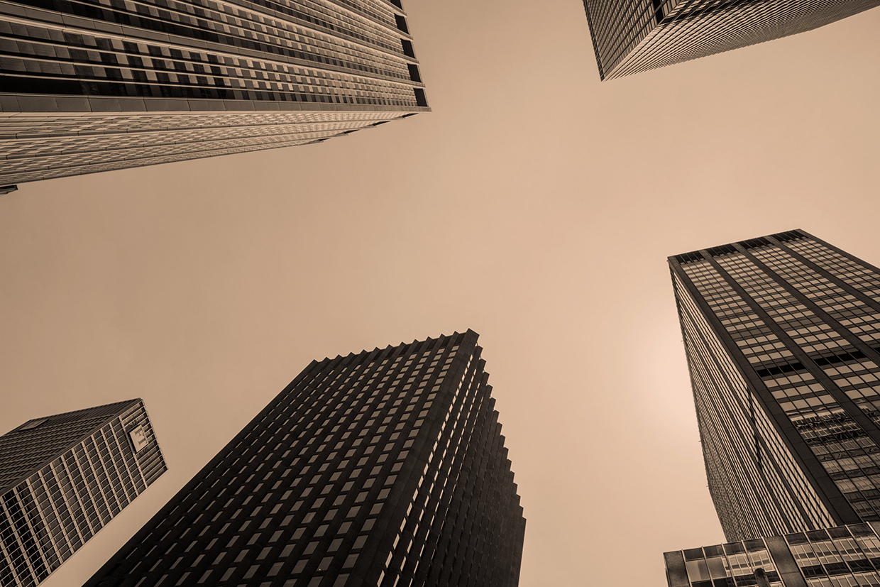 Upward view of several skyscrapers against a hazy sky, sepia-toned architectural photo, calm urban mood.